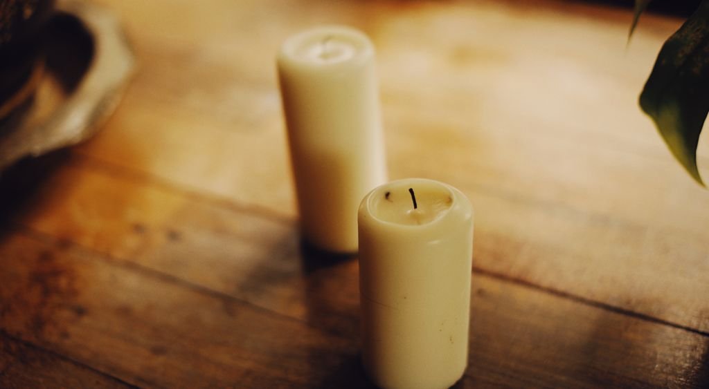 Due candele in cera avorio appoggiate su un piano in legno