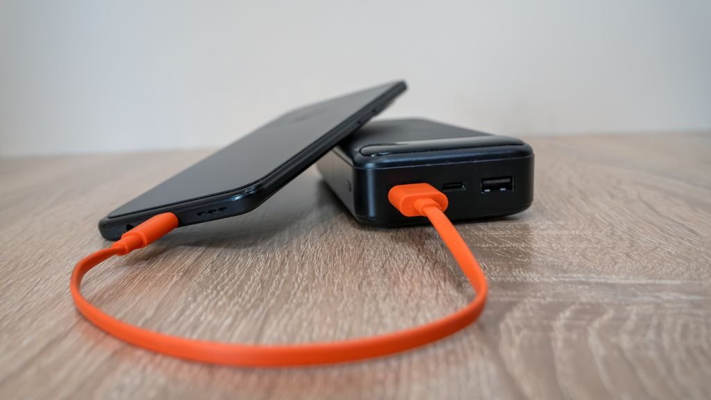 A power bank charging a smartphone with an orange cable on a desk