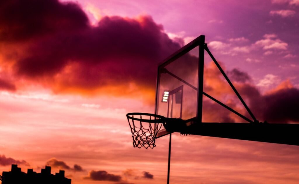 Basketball hoop silhouetted against a pink sunset sky