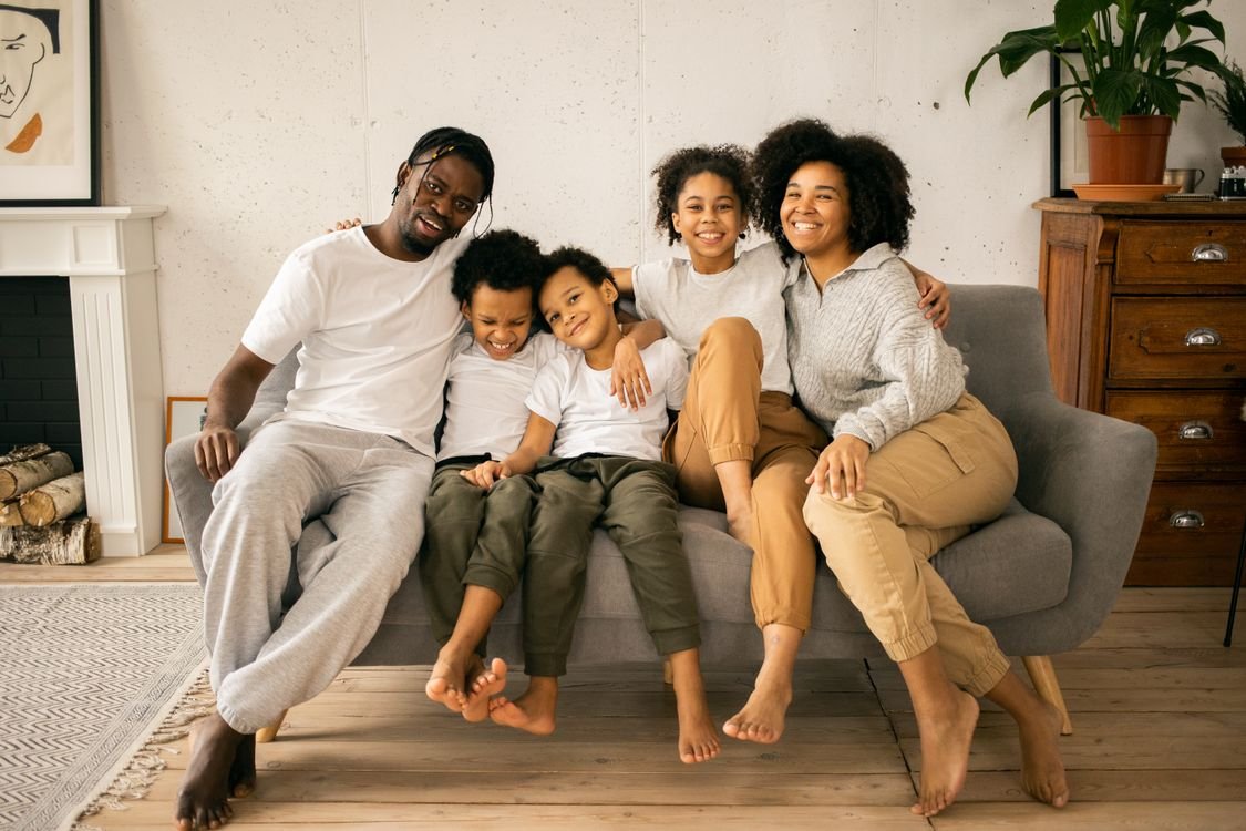 Family of five sitting together on a grey sofa in a bright living room