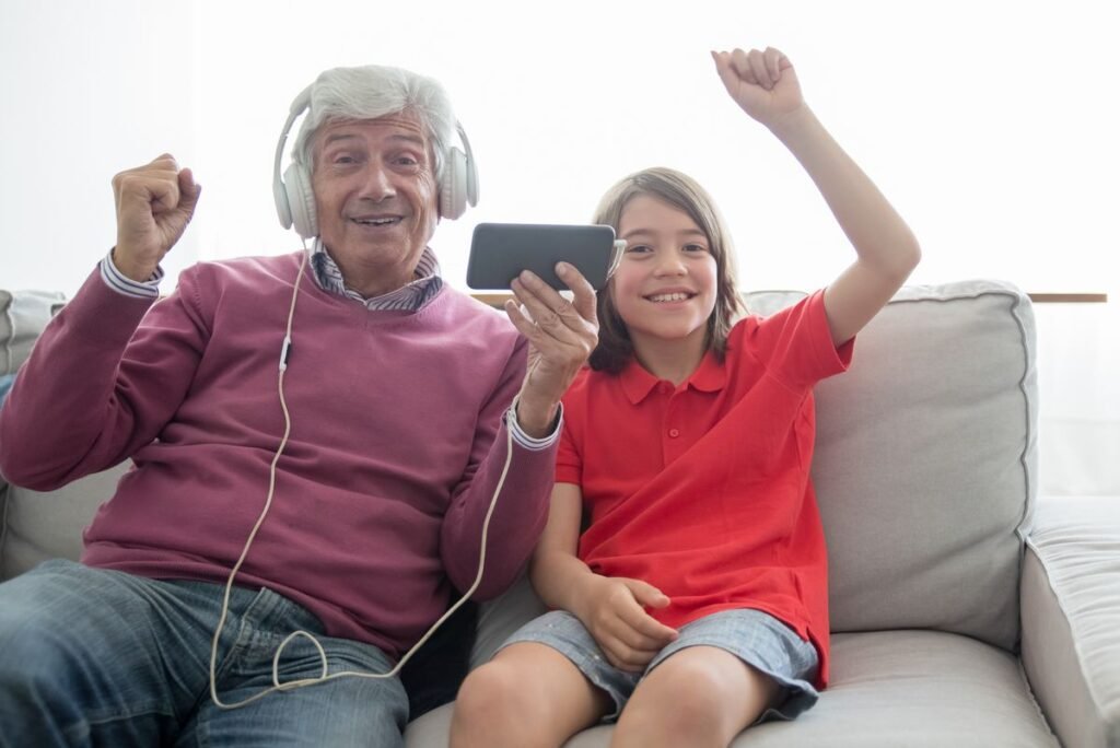 Grandfather and grandchild enjoying music with headphones on a sofa