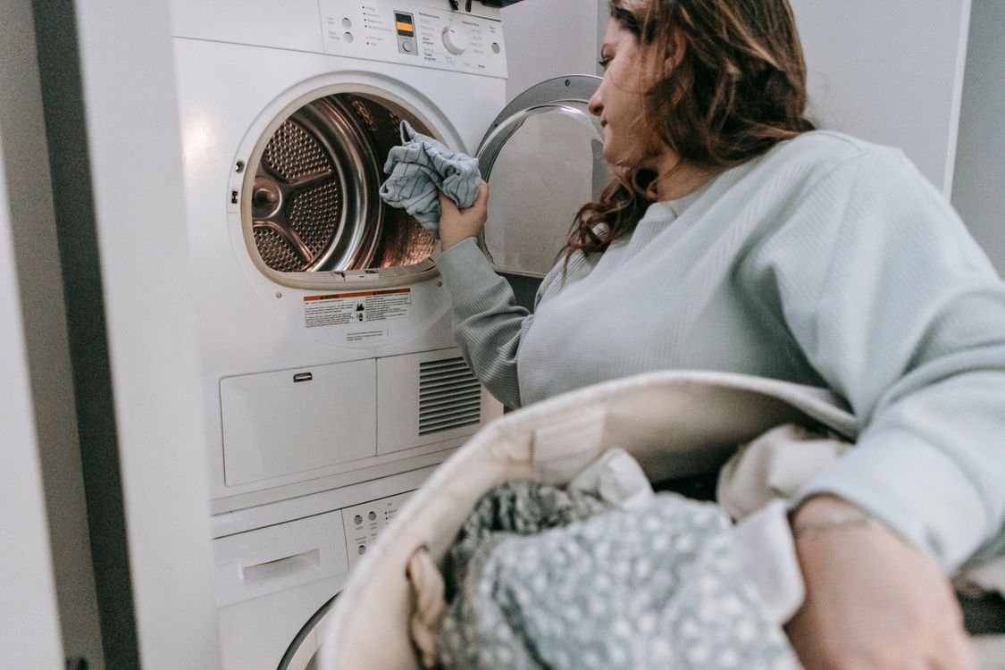 Woman loading laundry from a basket into a stacked front load washing machine