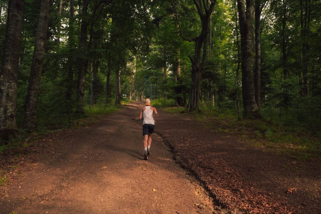 Trail Running Shoes Built for Muddy Climbs and Rocky Descents Runner on a forest dirt trail in summer light