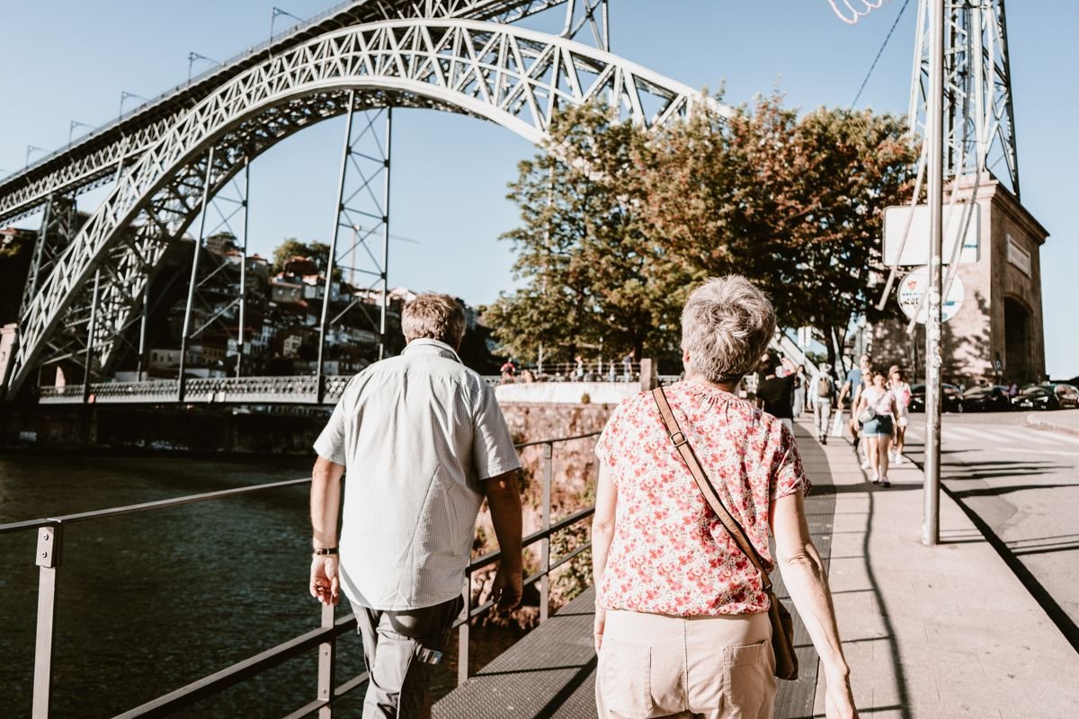 Older couple walking across an iron bridge on a sunny city trip