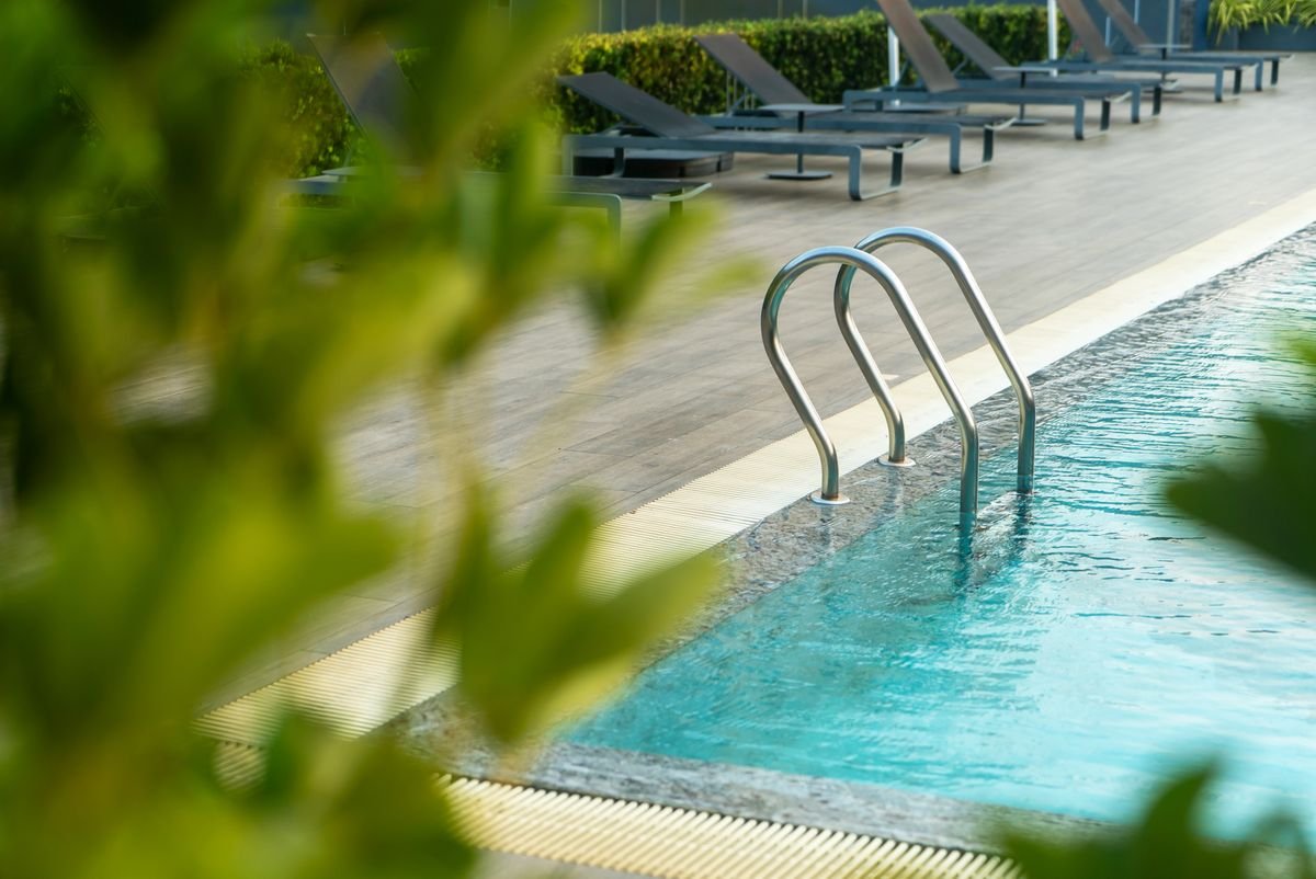 Pool edge with a handrail seen through garden foliage