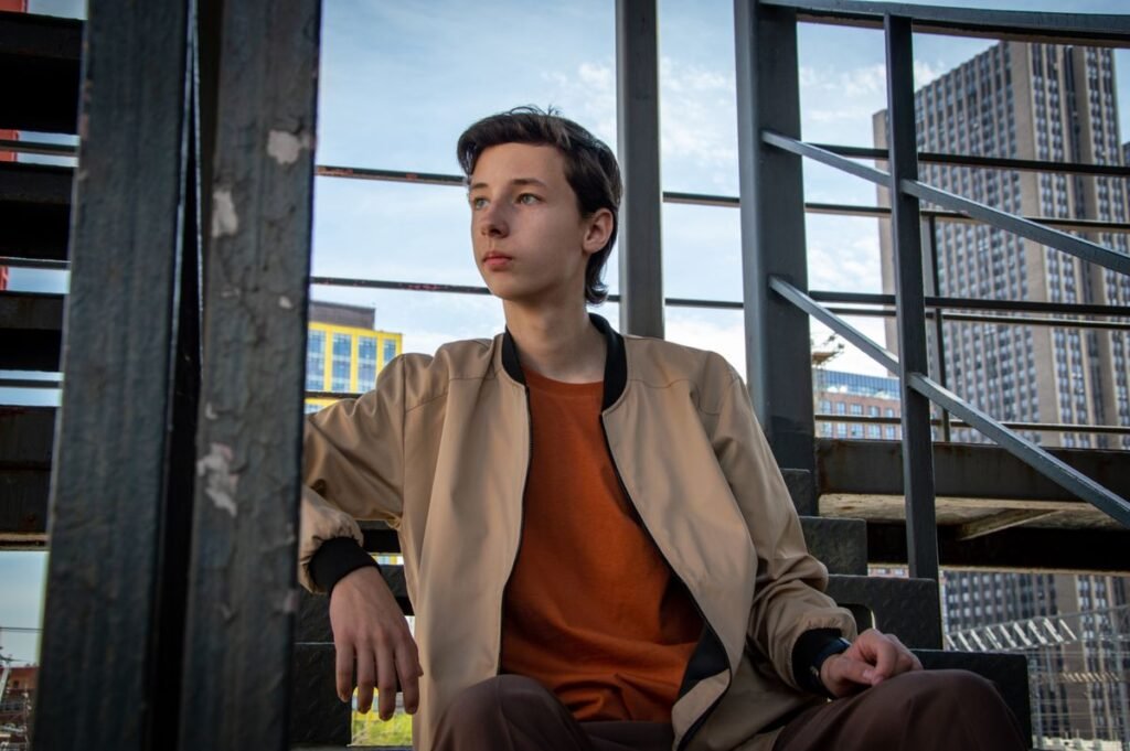 Man in a beige bomber jacket sitting on outdoor steps