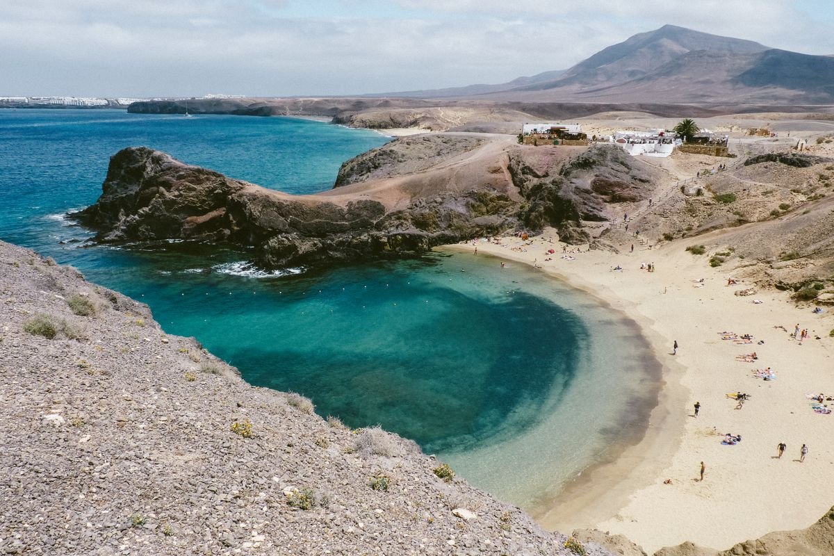 Turquoise cove with pale sand below volcanic cliffs